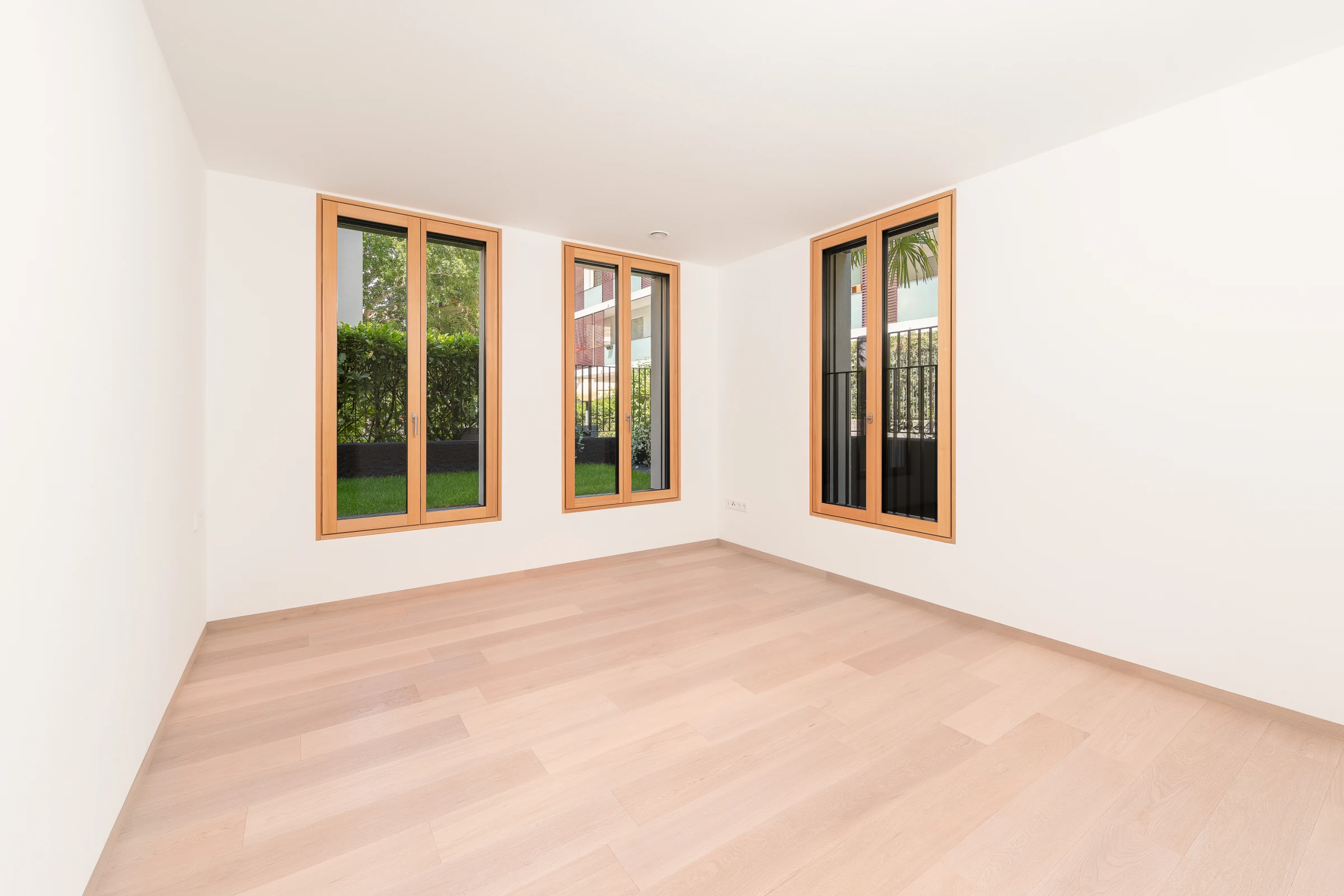 Helles Zimmer der Gartenwohnung mit drei großen Fenstern und Blick in den Garten